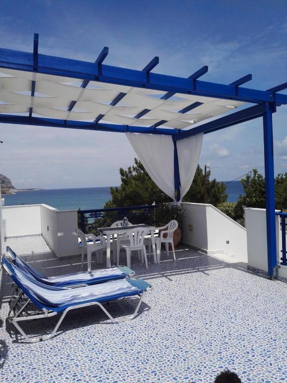 a patio with chairs and tables and a blue canopy at Bouganville Studios Stegna in Archangelos