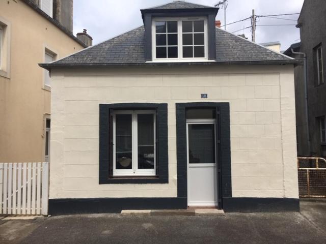 - un petit bâtiment blanc avec une fenêtre et une porte dans l'établissement La Crabette Bleue, à Grandcamp-Maisy
