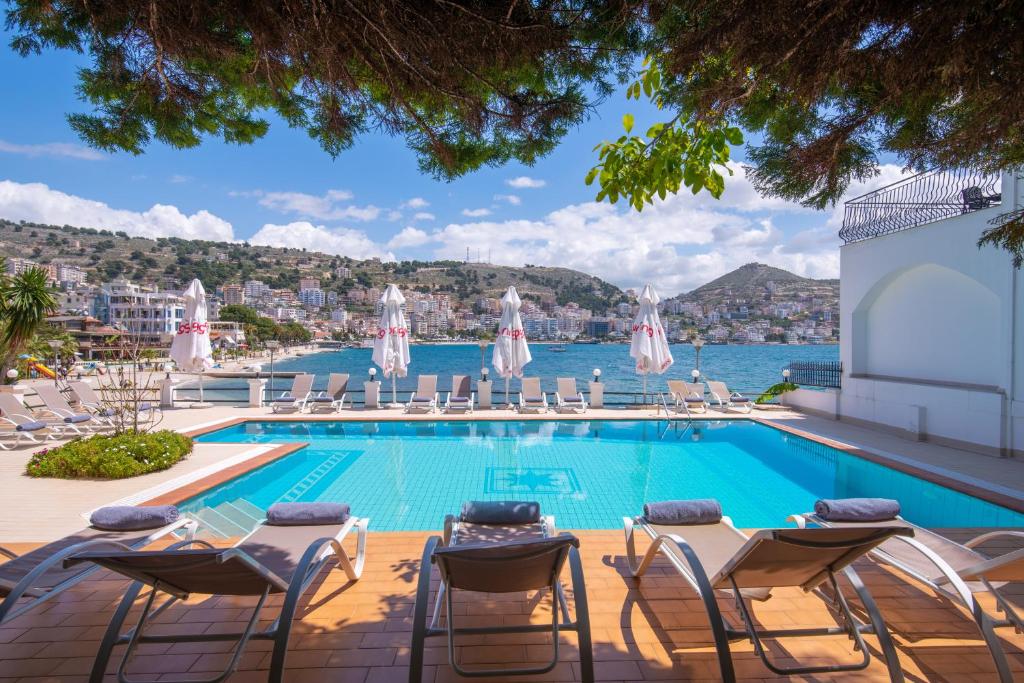 a swimming pool with chairs and a view of the water at PALMA city HOTEL in Sarandë