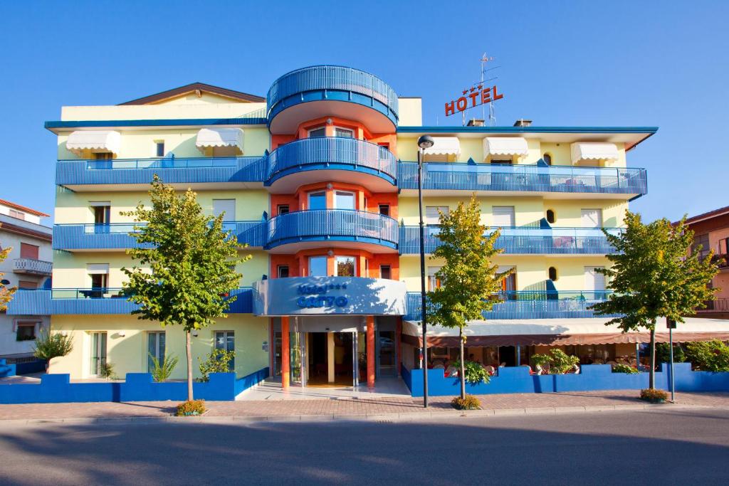 un edificio con balcones azules y árboles delante de él en Hotel Catto Suisse, en Caorle