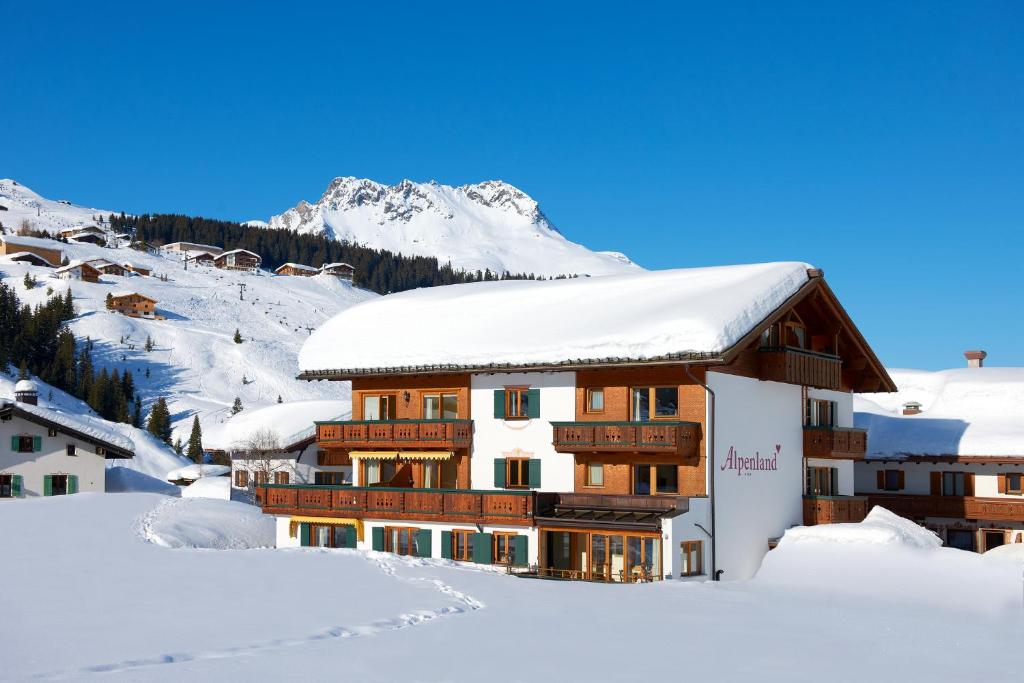 a building covered in snow with mountains in the background at Alpenland - Das Feine Kleine in Lech am Arlberg