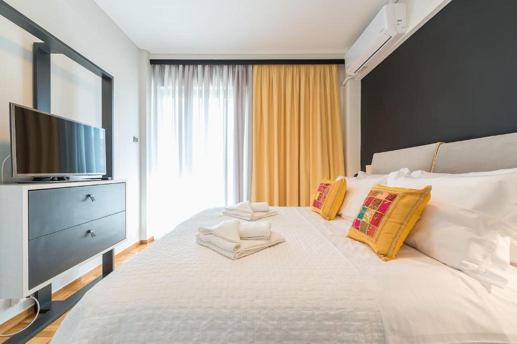 a bedroom with a large white bed with a flat screen tv at Seaside Central Apartment in Athens