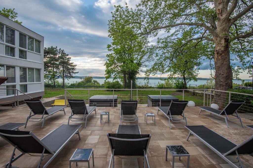 un patio con sillas, mesas y un árbol en Magaspart Panzió, en Balatonföldvár