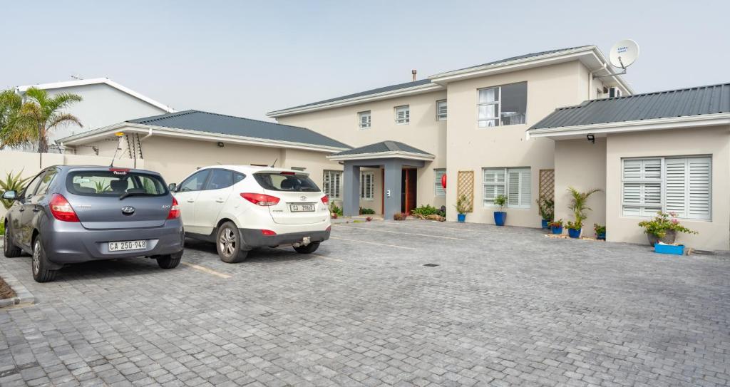 two cars parked in a parking lot in front of a house at Bentley's Guesthouse in Bloubergstrand