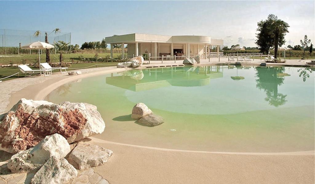 une grande piscine d'eau avec une maison en arrière-plan dans l'établissement Creative Design House Golf & SPA, à Pozzolengo