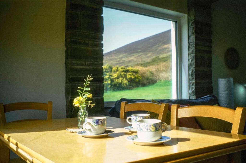 a table with cups and saucers on it with a window at Butterfly Cottage in Achill