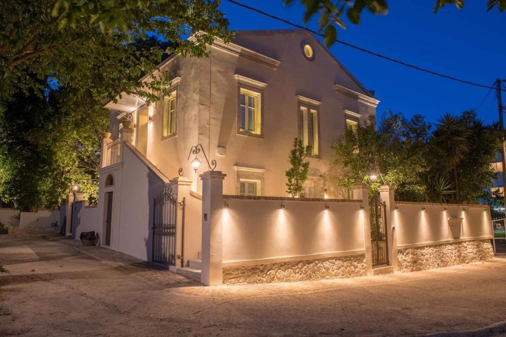 a white house with a fence at night at Carpofoli Corfu Town Serviced Luxury Suites in Corfu