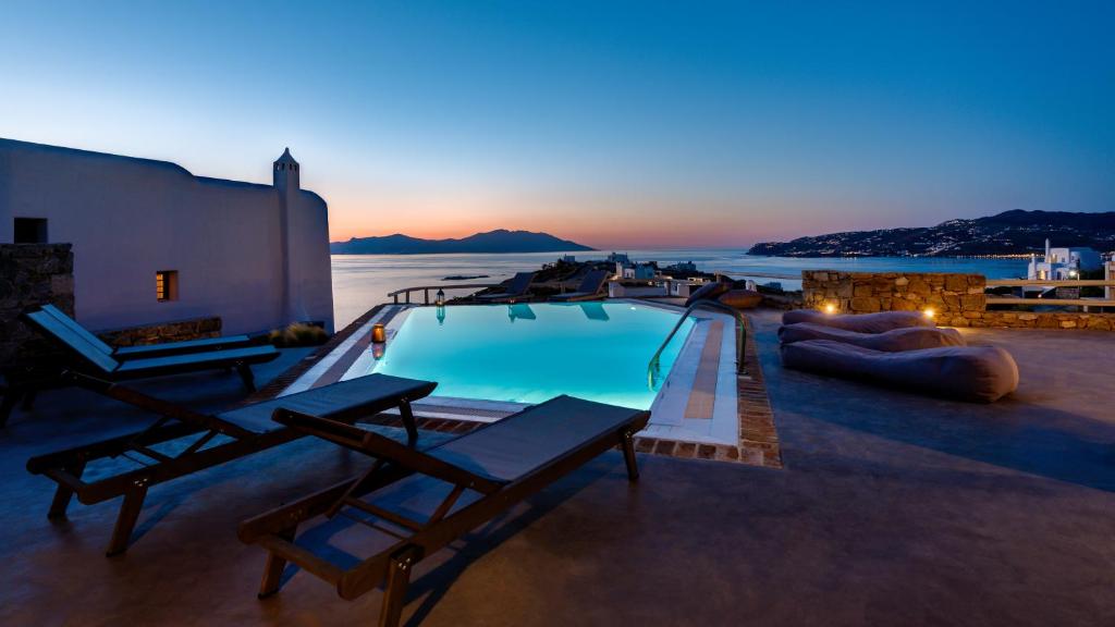 a swimming pool with chairs and the ocean at dusk at Villa Gin & Tonic by Mykonos Mood in Agios Ioannis Mykonos