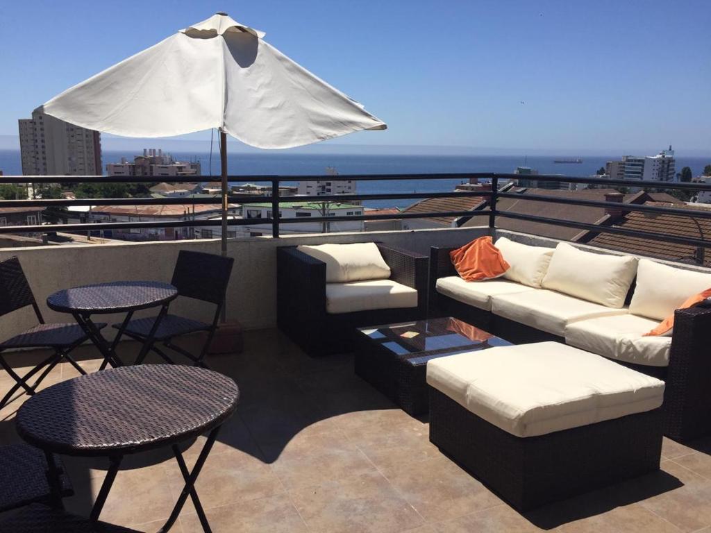um pátio no último piso com sofás, mesas e um guarda-chuva em B&B Hostel CasaMoro em Viña del Mar