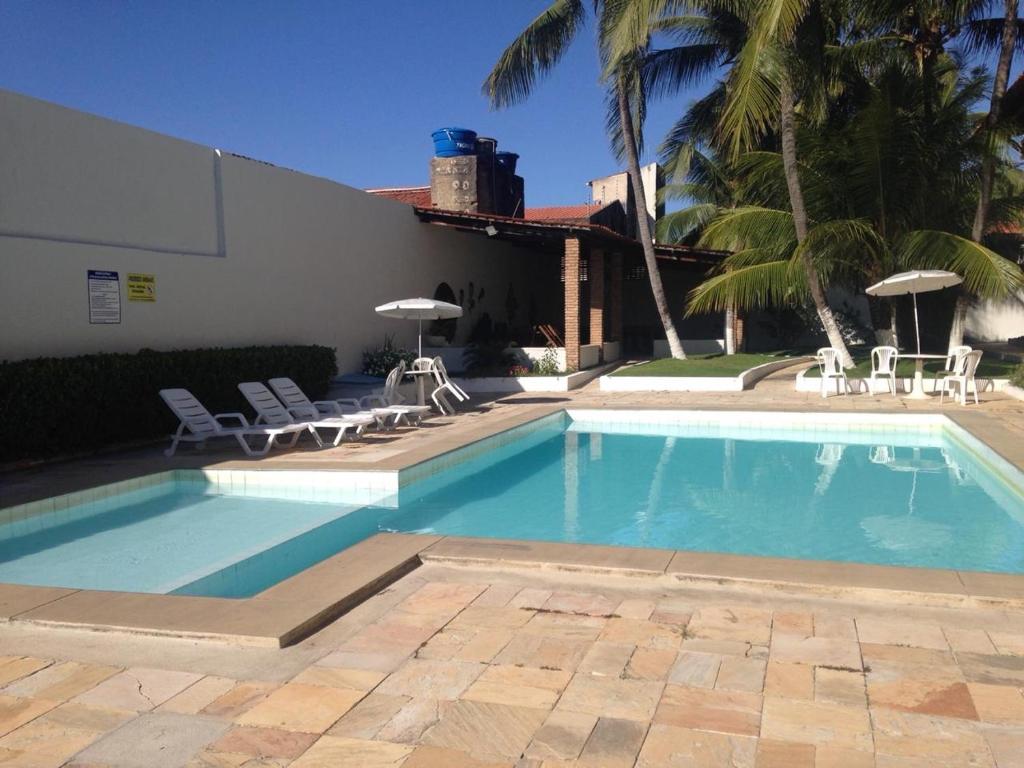 una piscina con sillas, un edificio y palmeras en Apto Cumaru 150m Do Mar Com Piscina en Praia do Frances