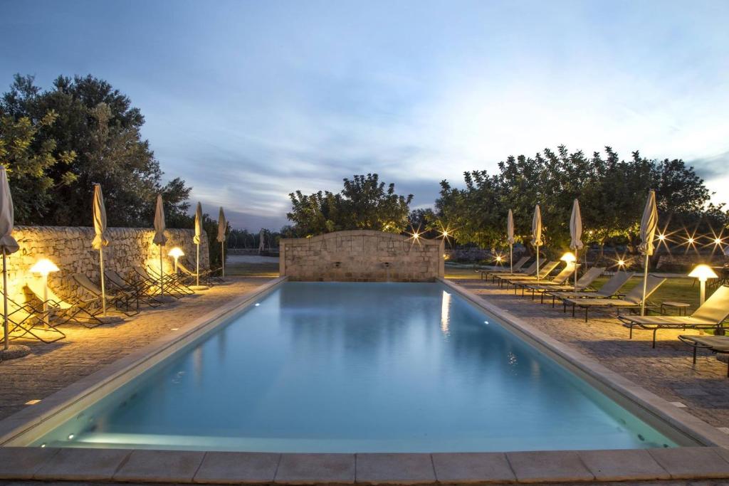 uma piscina com cadeiras e guarda-sóis à noite em Masseria Cianciò em Casa Serrafiori