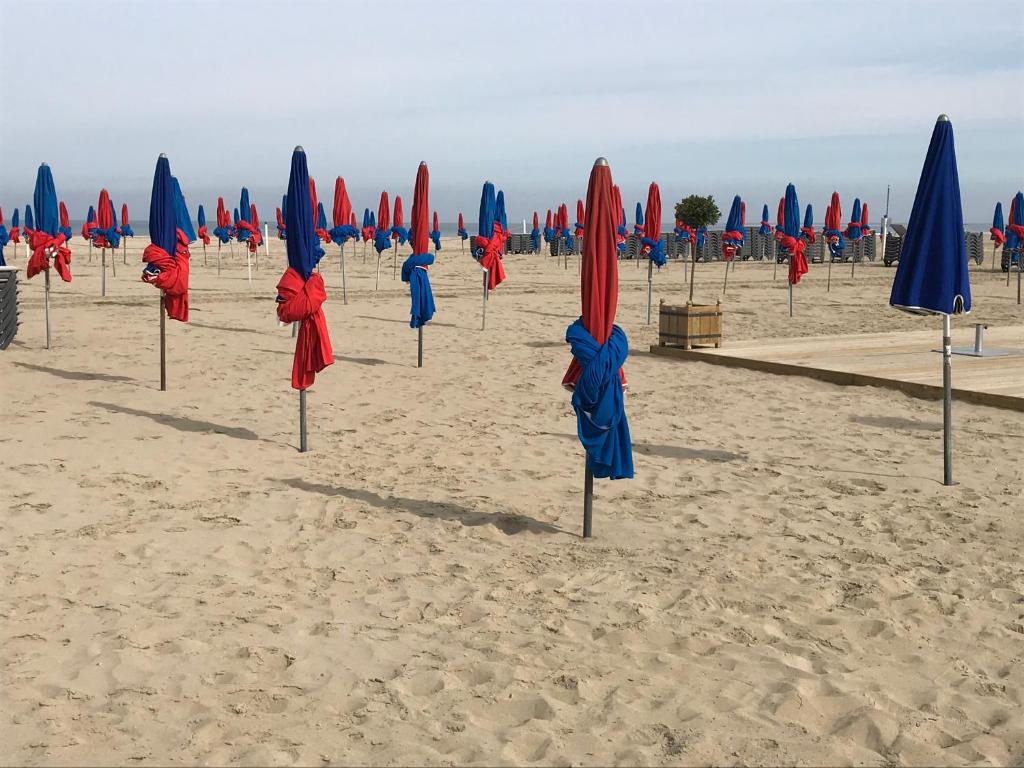 - un groupe de parasols bleus et rouges sur la plage dans l'établissement Appartement 3 chambres avec roof top à 5 mn de la plage, à Deauville
