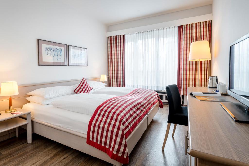 ザルツブルクにあるHotel IMLAUER & Bräuのベッド、デスク、テレビが備わるホテルルームです。