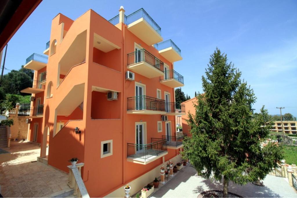 un grand bâtiment orange avec un arbre devant dans l'établissement Corfu Sunflower Apartments, à Benitses