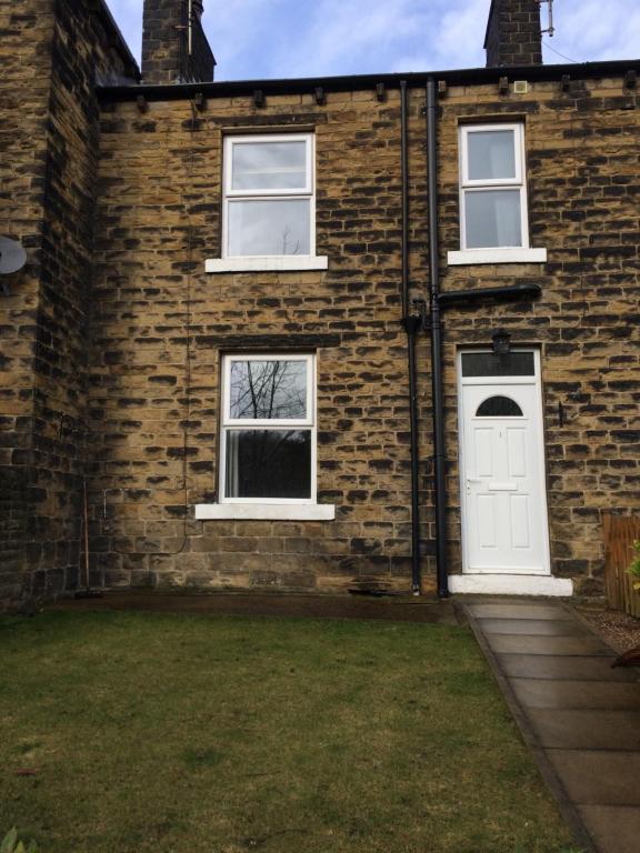 une maison en briques avec une porte blanche et deux fenêtres dans l'établissement SunnyBank, à Denby Dale