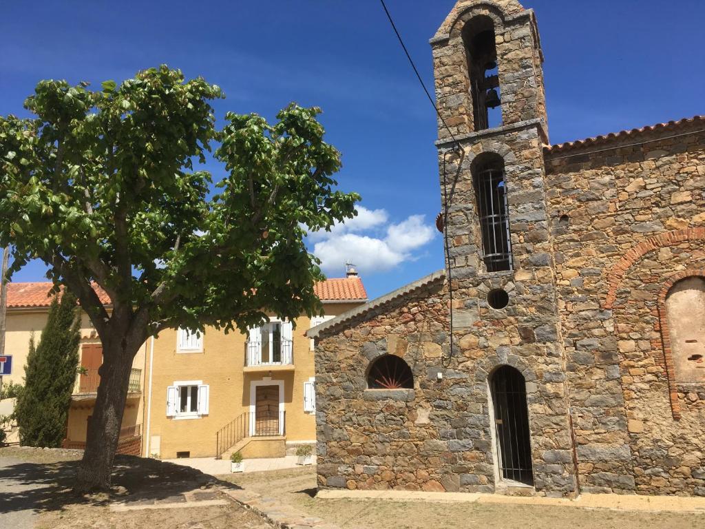 Una vieja iglesia de piedra con un árbol delante. en indé no, en Sari Solenzara