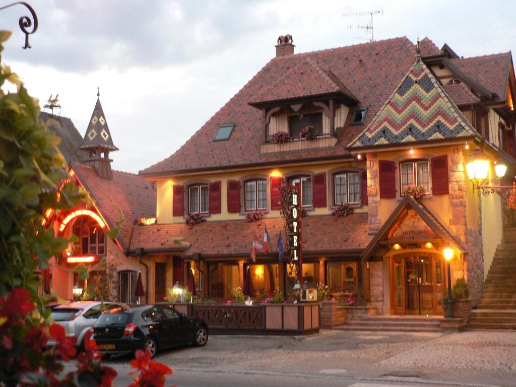 un grand bâtiment avec des voitures garées devant lui dans l'établissement Hôtel Le Mittelwihr, à Mittelwihr