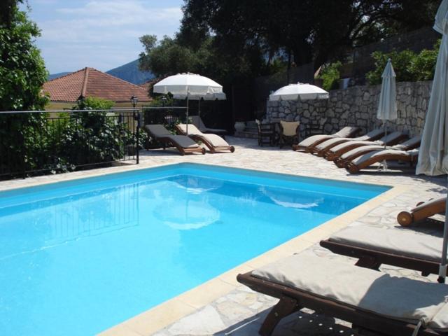 a large blue swimming pool with lounge chairs and umbrellas at Kiki Studios in Fiskardo