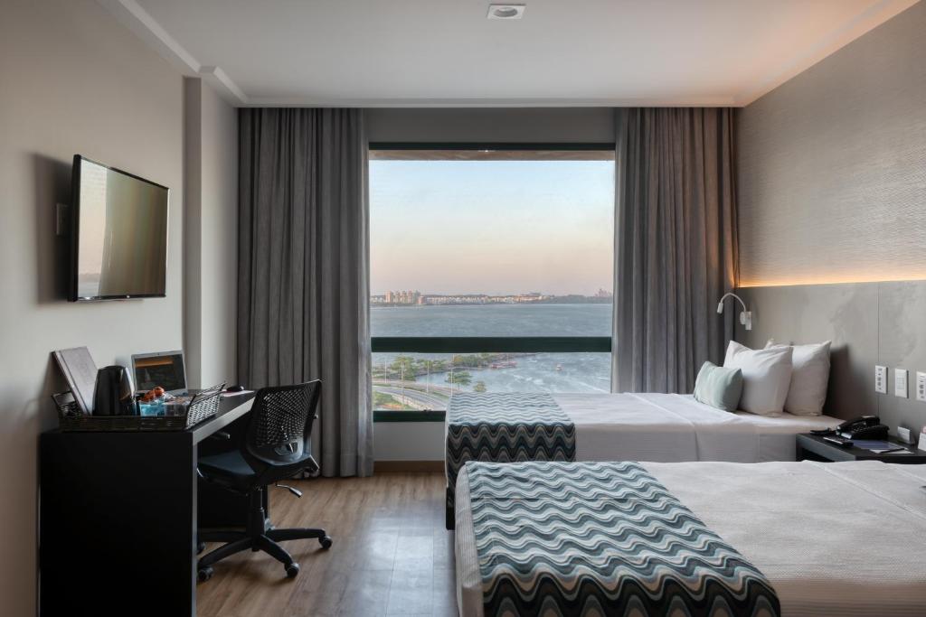 a hotel room with two beds and a desk and a window at Comfort Suítes Vitória in Vitória