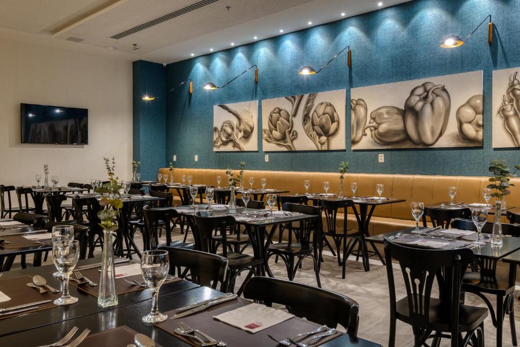a dining room with tables and chairs and paintings on the wall at Comfort Suítes Vitória in Vitória