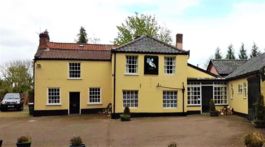 una casa amarilla con perros sentados fuera de ella en The Pelican Guesthouse en Ashwellthorpe