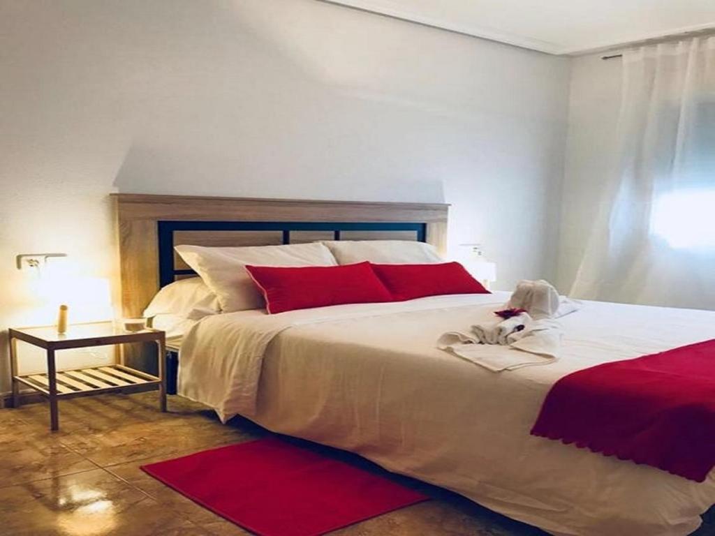 ロス・アルカサレスにあるAPARTAMENTO MANHATAN totalmente equipado CON PISCINA Y WIFI-CERCA A LA PLAYAのベッドルーム(赤い枕の大きな白いベッド付)