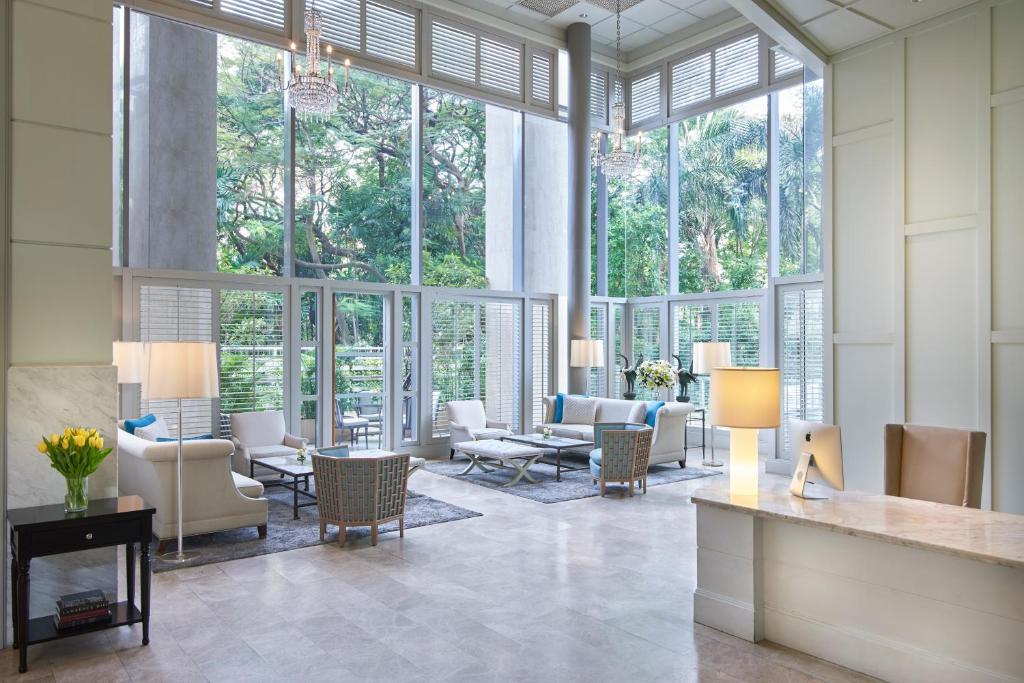 A glass-walled lounge is filled with daylight, greenery and seating.