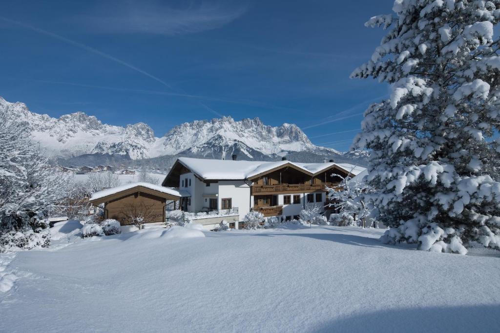 a house in the snow with mountains in the background at Appartements Schedererhaus in Going am Wilden Kaiser
