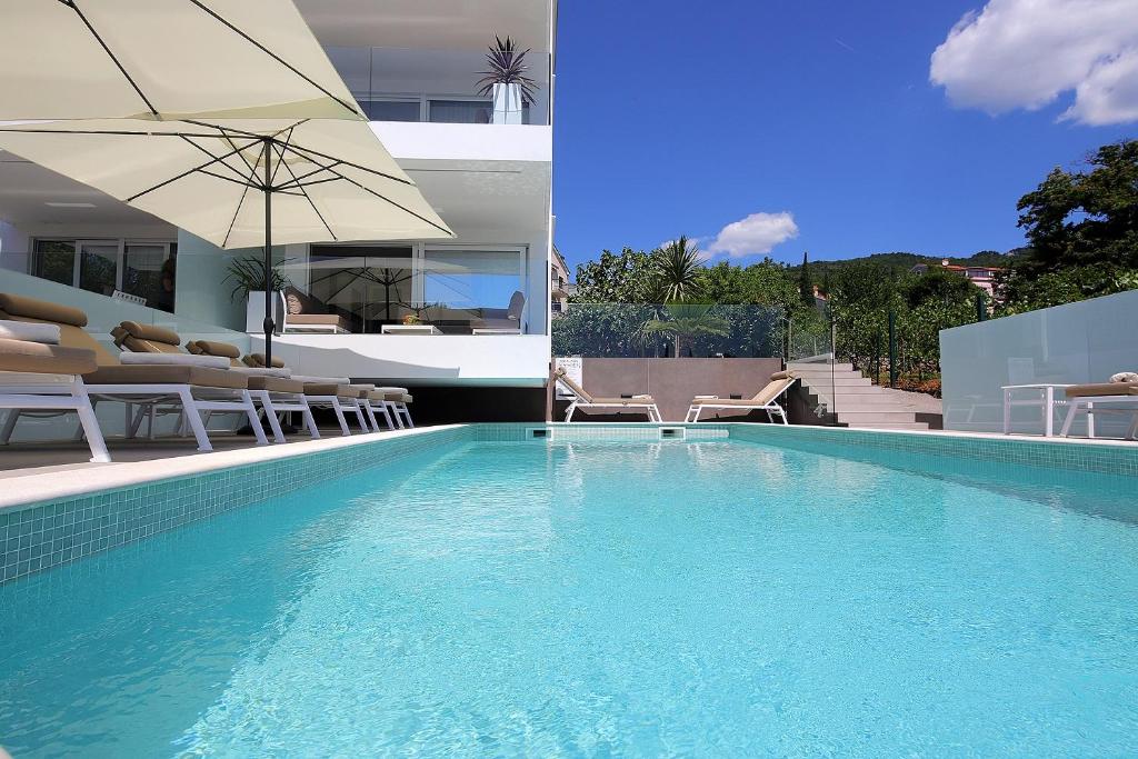 einen Pool mit Stühlen und einem Sonnenschirm neben einem Haus in der Unterkunft New apartment with swimming pool near the beach in Ičići