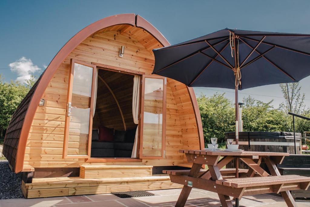 a small wooden cabin with a table and an umbrella at Wensleydale Glamping Pods in Redmire