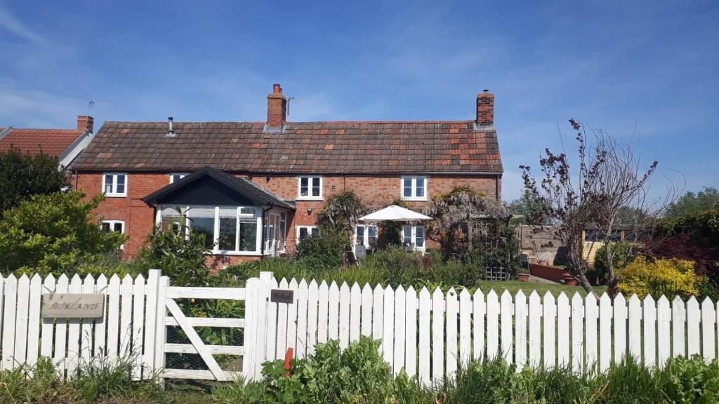 una cerca blanca frente a una casa de ladrillo rojo en Morland en Burrowbridge