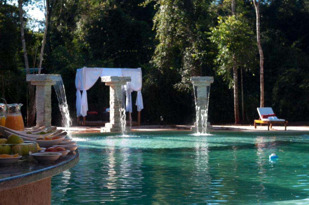 a pool with two water fountains and a table with fruit on it at Yvy Hotel de Selva in Puerto Iguazú