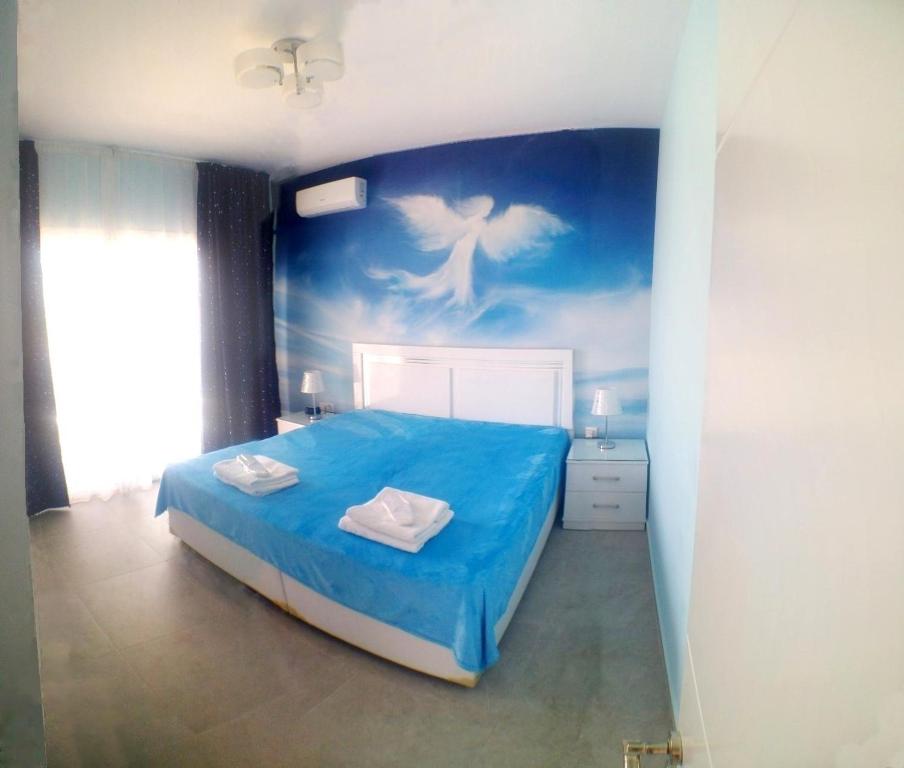 a bedroom with a blue bed with a painting on the wall at Angel's Apartment at Caesar Resort in Trikomo