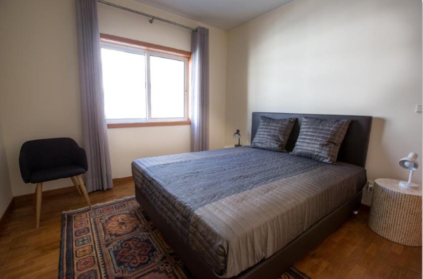 ein Schlafzimmer mit einem Bett, einem Fenster und einem Stuhl in der Unterkunft Afife T2 - Bouça Cabrita Residence in Afife