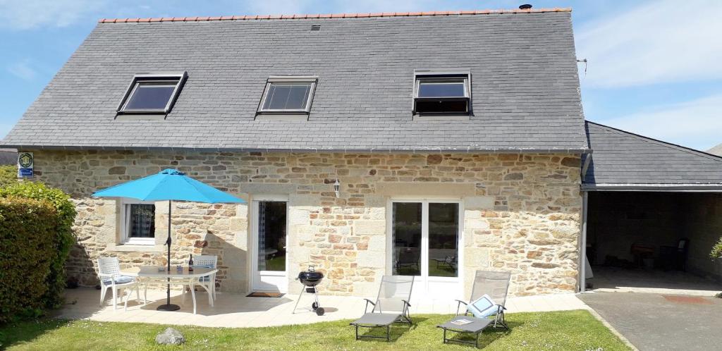 Casa de piedra con mesa, sillas y sombrilla en Maison sur jardin clos au calme à la campagne et proche des plages, en Mahalon