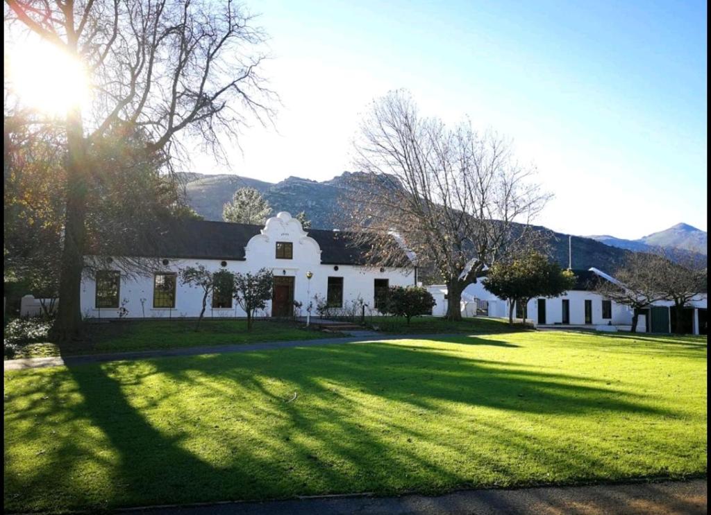 a white house with a large yard with the sun shining at Le Arc Manor House in Franschhoek