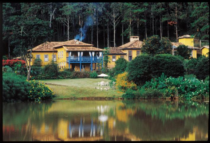 una gran casa amarilla junto a un cuerpo de agua en Hotel Fazenda Santa Marina en Santana dos Montes