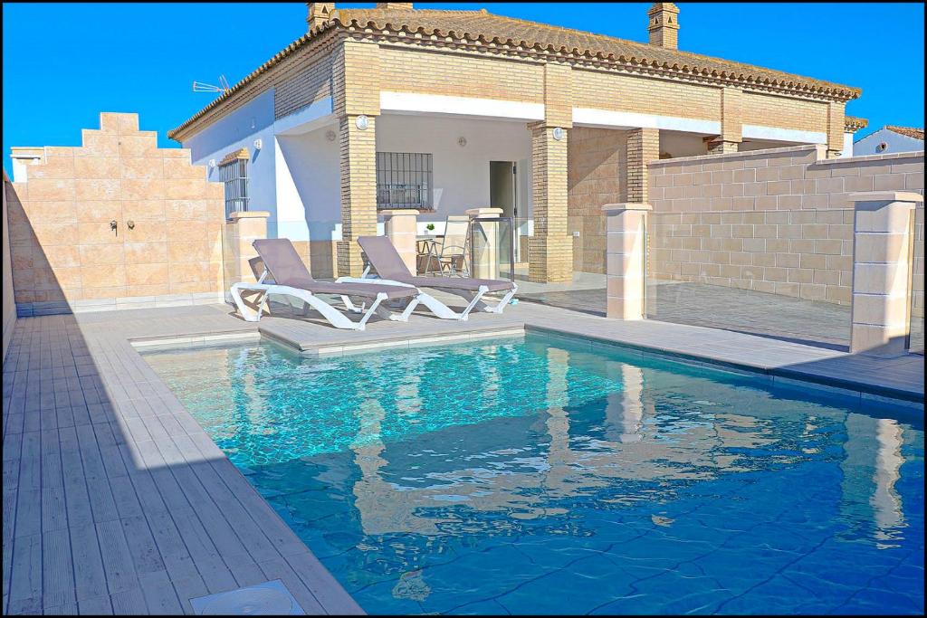 una piscina con due sedie e una casa di Chalet Peñuelas con piscina a Conil de la Frontera
