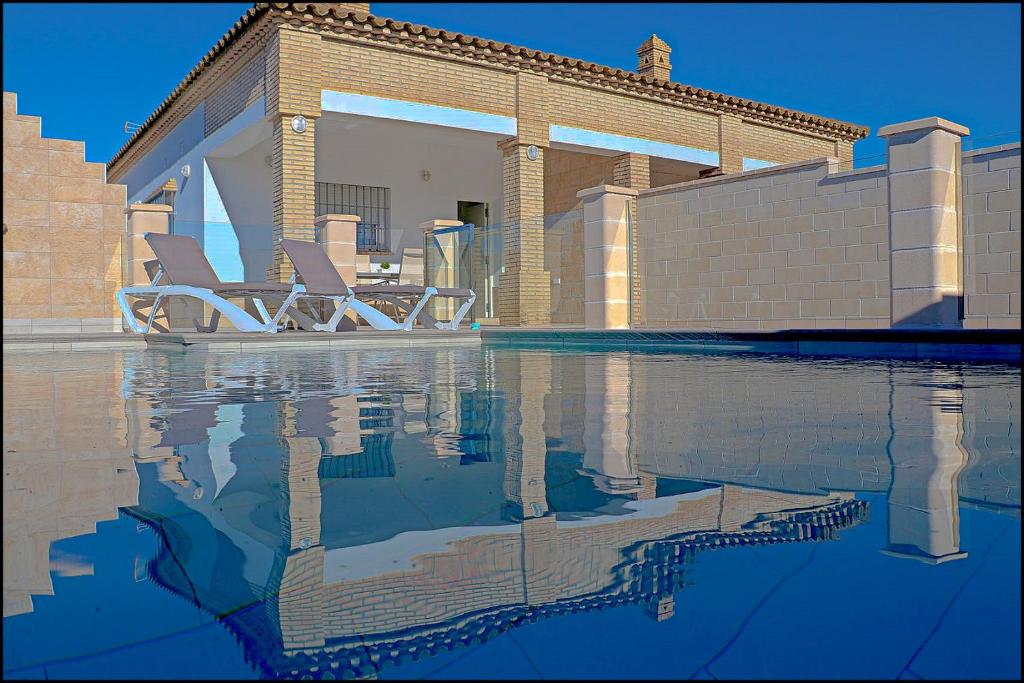 una piscina con due sedie a sdraio accanto a una casa di Chalet Peñuelas con piscina a Conil de la Frontera