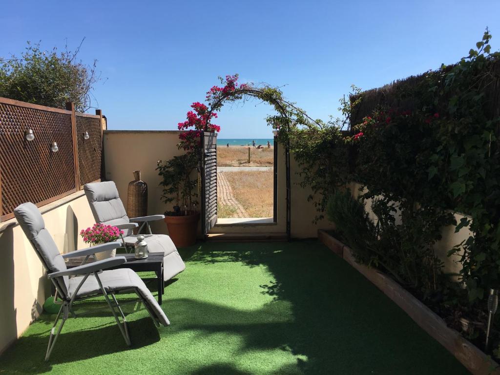 un patio con 2 sedie, un tavolo e una porta aperta di Beach flat with garden a Castelldefels