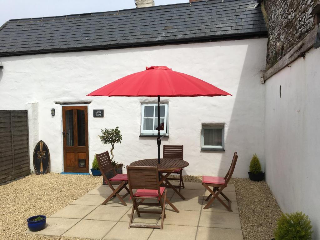 une table avec un parapluie rouge devant une maison dans l'établissement Little Barn, Greendale Farm, à Barnstaple