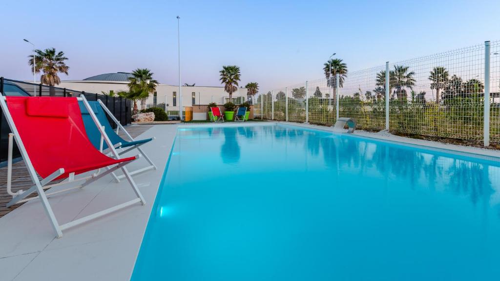 - une piscine avec une chaise rouge et une piscine bleue dans l'établissement The Originals City, Hôtel Les Dômes, Perpignan Sud Saleilles, à Perpignan