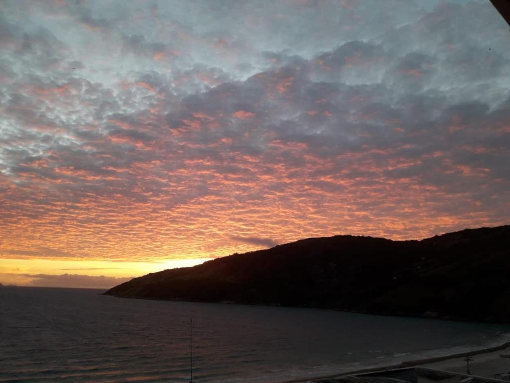 una puesta de sol sobre un cuerpo de agua con una montaña en Praia Linda Hospedagem, en Arraial do Cabo