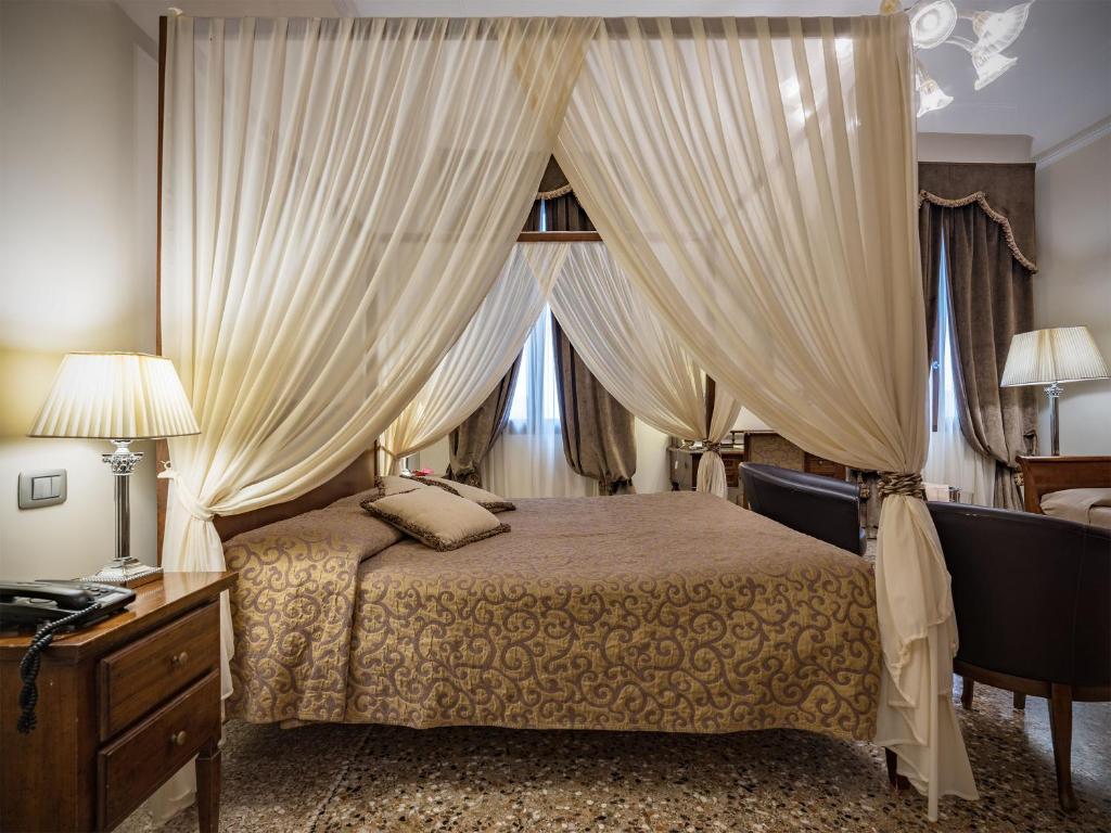a bedroom with a bed with curtains and a desk at Hotel Dell'Opera in Venice
