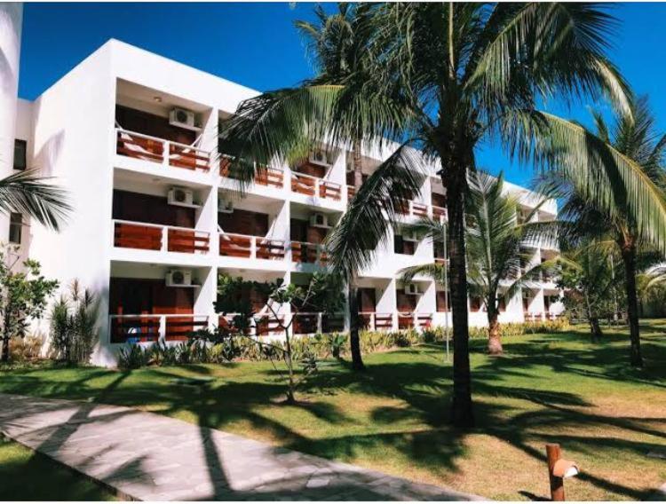 a large white building with palm trees in front of it at Hotel Village Porto de Galinhas - Apartamento 215 in Porto De Galinhas