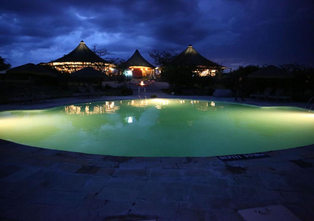 uma piscina de água verde à noite com cabanas ao fundo em AA Lodge Maasai Mara em Talek