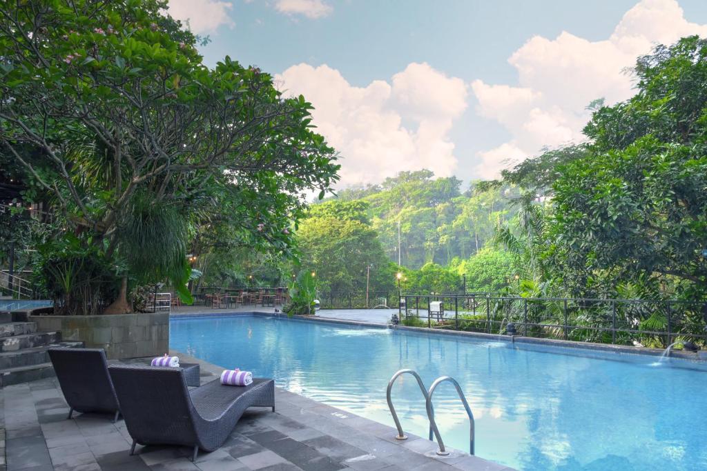 a large swimming pool with two chairs and trees at Oak Tree Emerald Semarang in Semarang