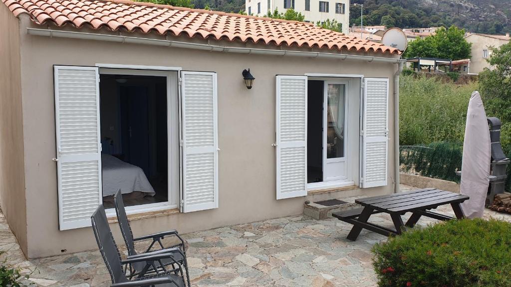 een klein huis met witte luiken en een picknicktafel bij Gîte A l'ombre du clocher in Calenzana