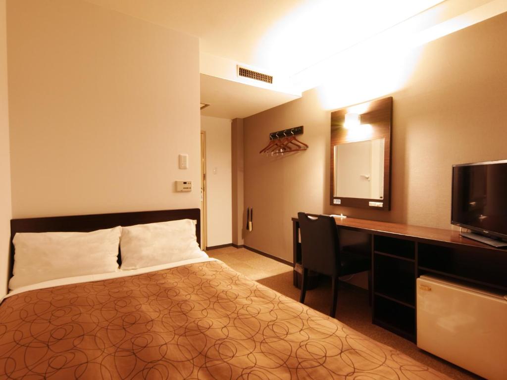 熊本市にある熊本グリーンホテルのベッド、デスク、テレビが備わるホテルルームです。