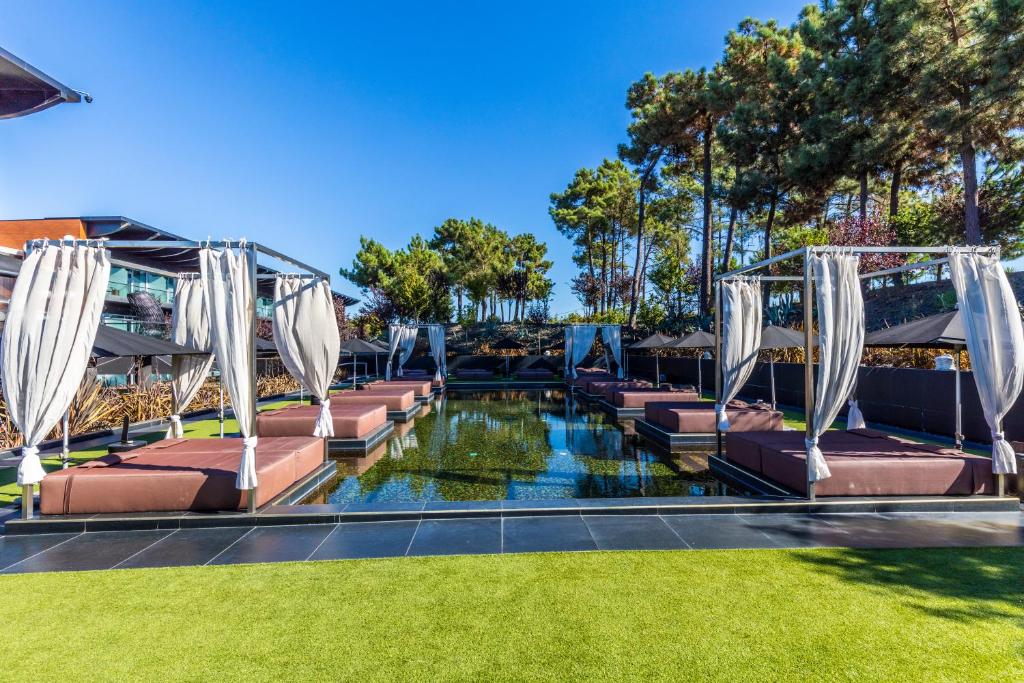 a swimming pool with benches and a pond with trees at Evidencia Belverde Hotel in Amora
